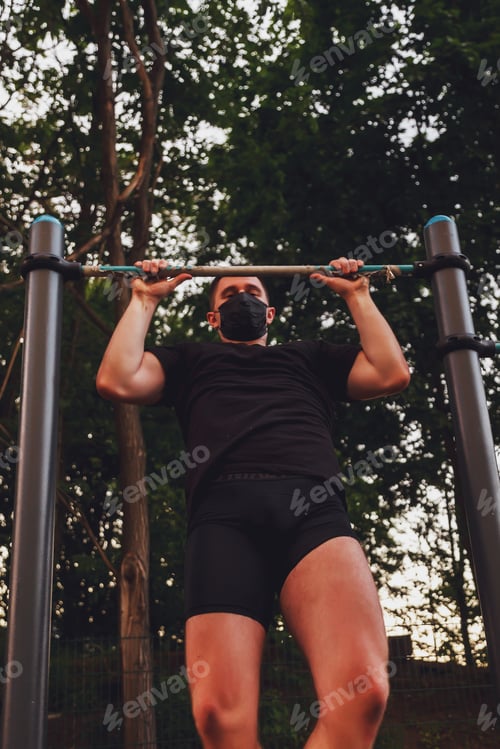 Preview: Young guy, athlete pulls on bar. He's wearing black medical mask