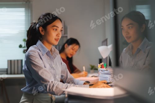 Preview: Asian businesswomen working late in office with computer and documents