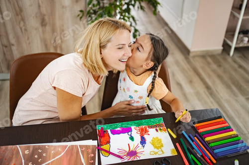 Preview: Cute girl kisses her mother while they both work on vibrant art projects