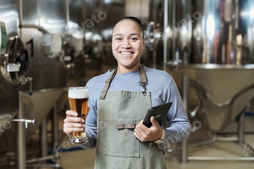 Preview: Smiling woman holding beer glass at brewing factory