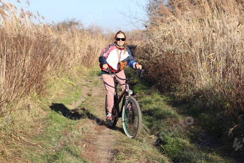 Preview: A young woman is riding a bike on a sunny day on a country road.