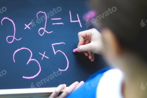 Preview: Top view of schoolgirl in glasses doing sums writing on blackboard by chalk