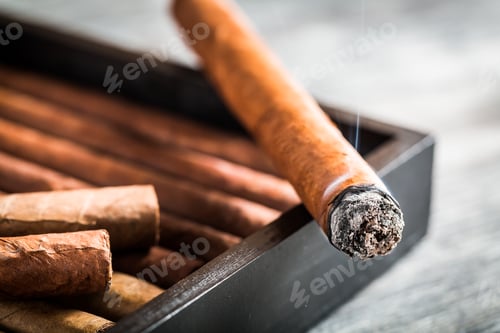 Preview: Burning cigar with smoke on wooden humidor