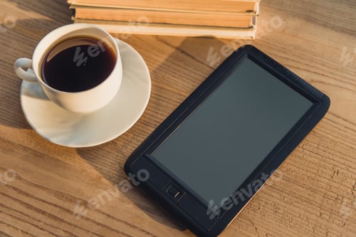 Preview: black e-reader with blank screen lying near cup with coffee on table