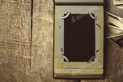 Preview: Old book with empty photo frame on wooden table with loose photographs scattered around