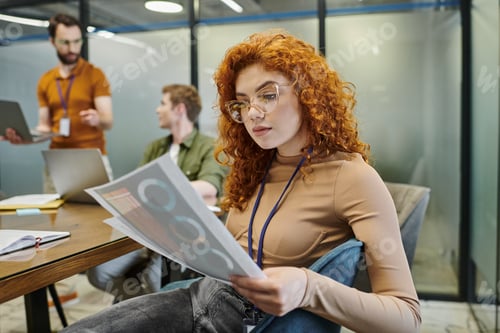 Preview: thoughtful redhead businesswoman with infographics, blurred colleagues talking in modern office