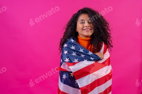 Preview: Portrait of a curly-haired woman smiling with the usa flag on a pink background, studio shot