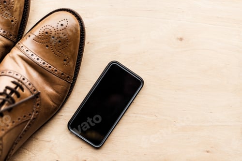Preview: top view of smartphone and brown leather shoes on wooden surface