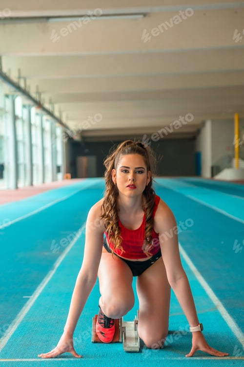 Preview: Indoor athletics, portrait of female sprinter preparing the start of the race in training