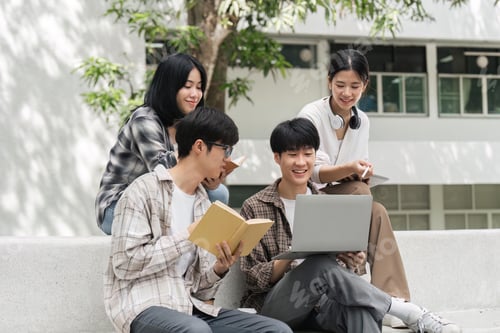 Preview: Group of happy students checking results on laptop and tablet while sitting on college campus