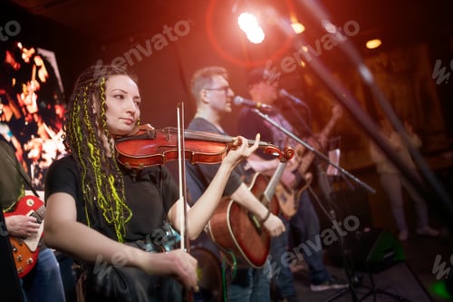 Preview: A female violinist plays the violin. Band performs on stage, rock music concert.