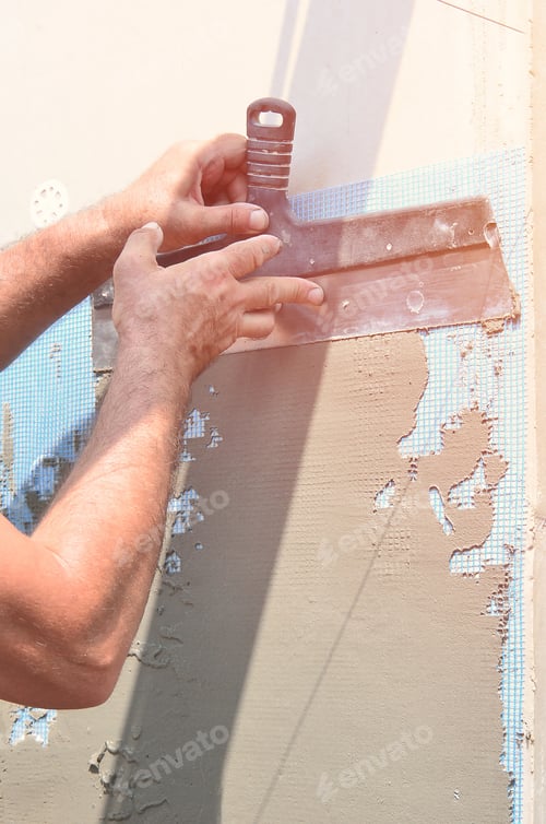 Preview: Hands of an old manual worker with wall plastering tools renovating house