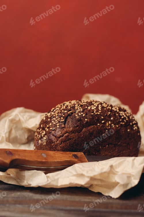 Preview: rye bread on paper packaging on a red background and a wooden table with a sharp knife