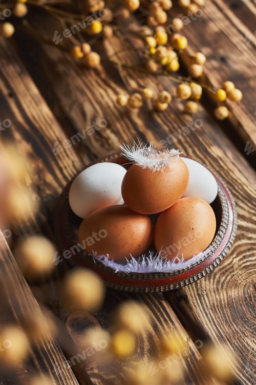 Preview: White and brown easter eggs with feather in a bowl on dark wooden table.