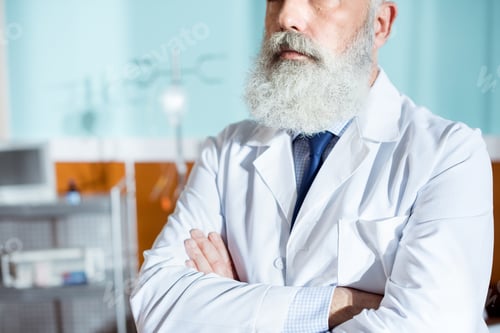Preview: Midsection view of senior bearded doctor standing with hands crossed