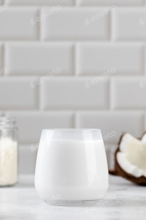 Preview: Fresh coconut milk in glass with sliced coconut and white tile background. Alternative milk
