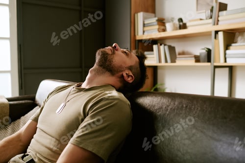 Preview: Young Adult Caucasian Man Leaning Back on Sofa Appearing Emotionally Exhausted
