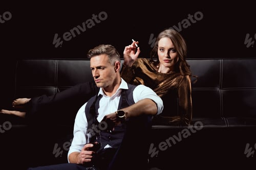 Preview: attractive woman lying on couch with cigarette while handsome man holding glass of red wine isolated