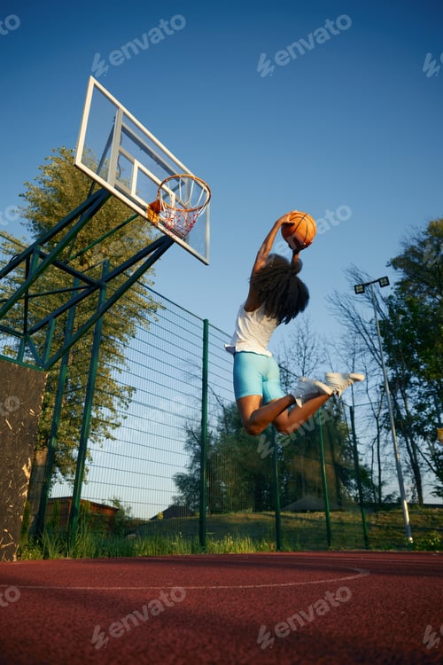 Preview: Young woman basketball player frozen in motion jumping high making slam dunk
