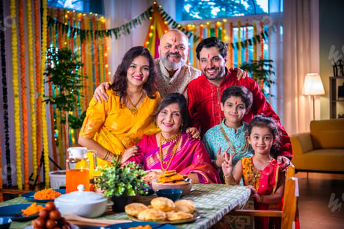 Preview: Portrait of happy Indian family in traditional outfit celebrating Diwali at home eating food