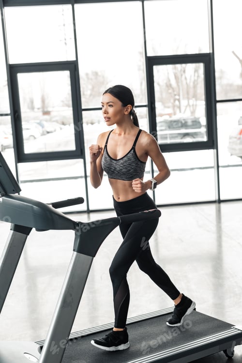 Preview: beautiful young sportswoman running on treadmill in gym