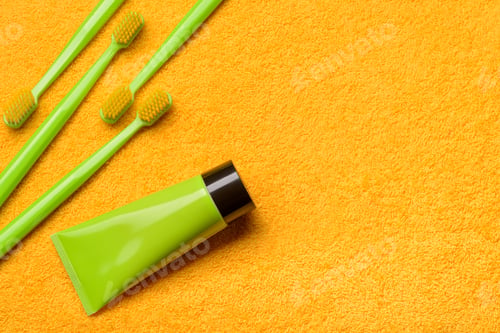Preview: Green toothbrushes with paste tube on yellow bath towel. Importance of oral health care.