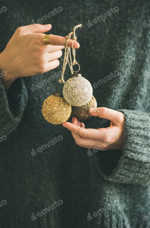 Preview: Woman in grey sweater holding decorative golden balls in hands