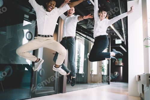 Preview: Business team celebrating success by jumping together in office