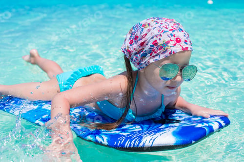 Preview: Little adorable girl on a surfboard in the turquoise sea