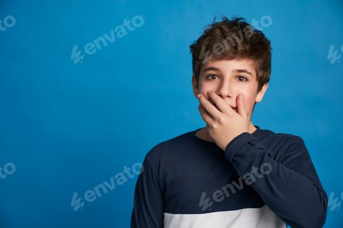 Preview: Portrait of surprised boy making hand gesture near mouth isolated on blue background.