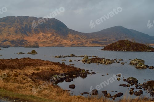 Preview: Overcast sky above a serene lake dotted with rocks and surrounded by rolling hills, Scotland