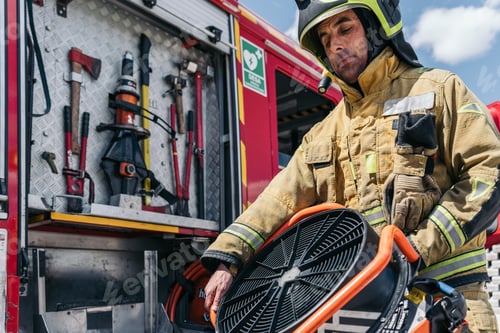 Preview: Firefighter holding ventilation fan at fire station with fire truck in background