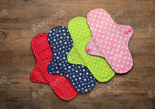 Preview: Many reusable cloth menstrual pads on wooden table, flat lay