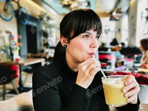 Preview: Portrait of beautiful young woman in cafe. Attractive millennial drinking fresh juice.