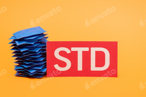 Preview: stack of condoms near paper with std lettering isolated on orange