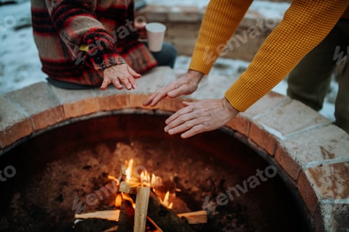 Preview: Senior couple sitting and heating together at outdoor fireplace in winter evening.