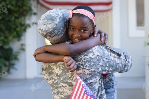 Preview: African american soldier father hugging smiling daughter holding flag in front of house