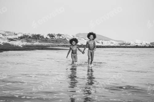 Preview: Two african american twin sisters running inside the water on the beach during summer time