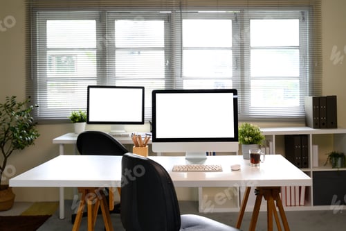 Preview: Home office interior with desktop computers on white desks and natural light from large windows