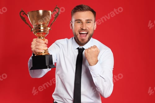 Preview: Portrait of happy young businessman with gold trophy cup on red background