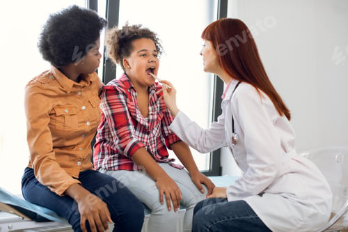 Preview: Mom and daughter at doctor's office. Caucasian doctor gp pediatrician, examining throat of cute