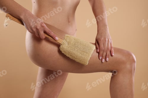 Preview: Woman doing anti cellulite massage with loofah on beige background, closeup