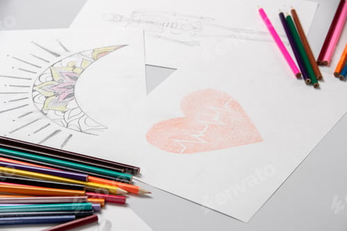Preview: Drawing a painting of a red heart and a moon on the paper laying on the table with pencils