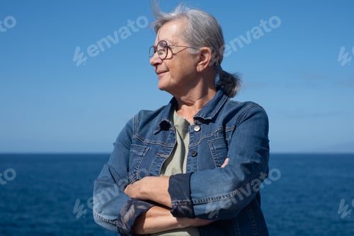 Preview: Portrait of alone caucasian elderly woman with crossed arms standing on the rocky beach