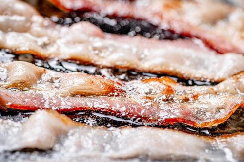 Preview: Pieces of bacon are fried in boiling oil with air bubbles.