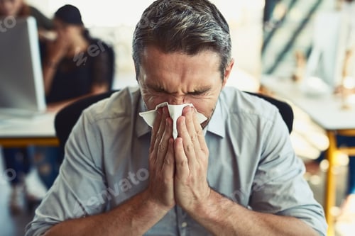 Preview: Allergies are just the worst. Shot of a businessman blowing his nose in an office.