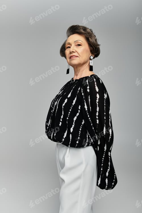 Preview: A graceful woman in her 60s radiates confidence in stylish attire against a grey backdrop.