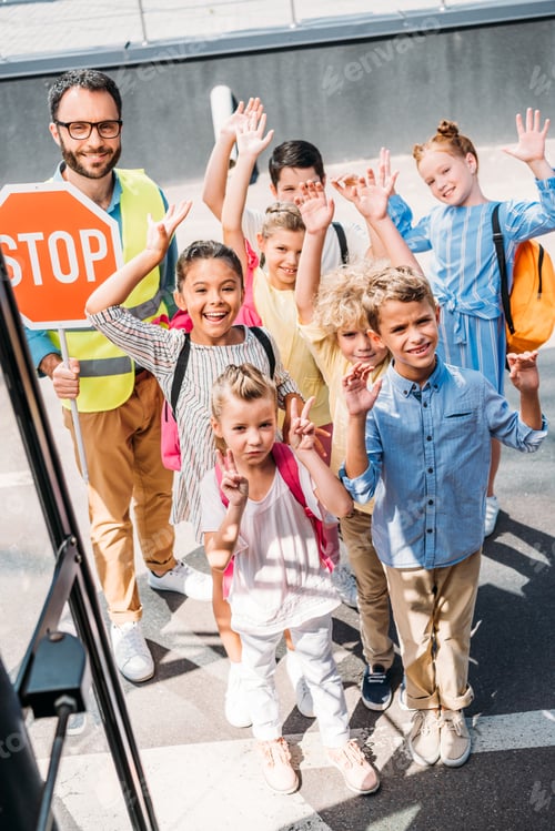 Preview: view from school bus at group of scholars with traffic guard looking at camera and waving