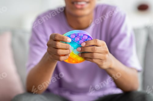 Preview: Closeup view of African American teenager playing with antistress POP IT toy at home