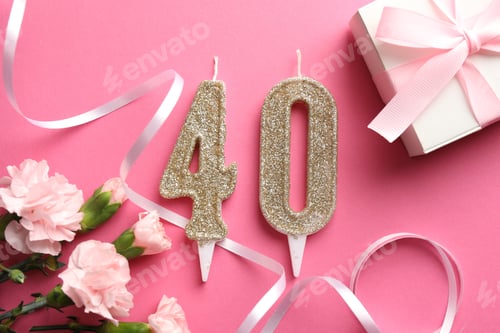 Preview: 40th birthday. Number shaped candles, gift and flowers on pink background, flat lay